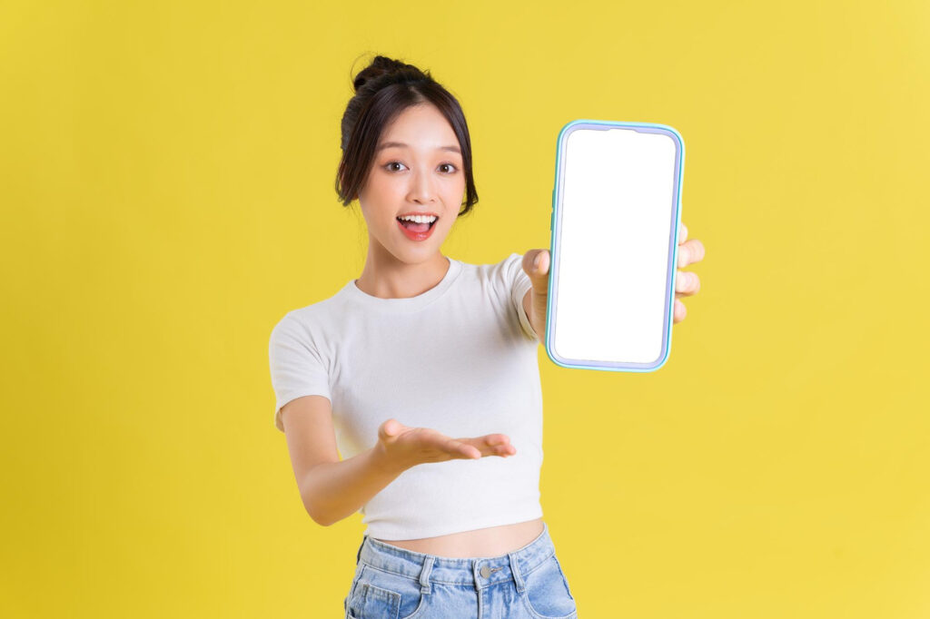 young-asian-woman-holding-phone-with-cheerful-face-yellow-background